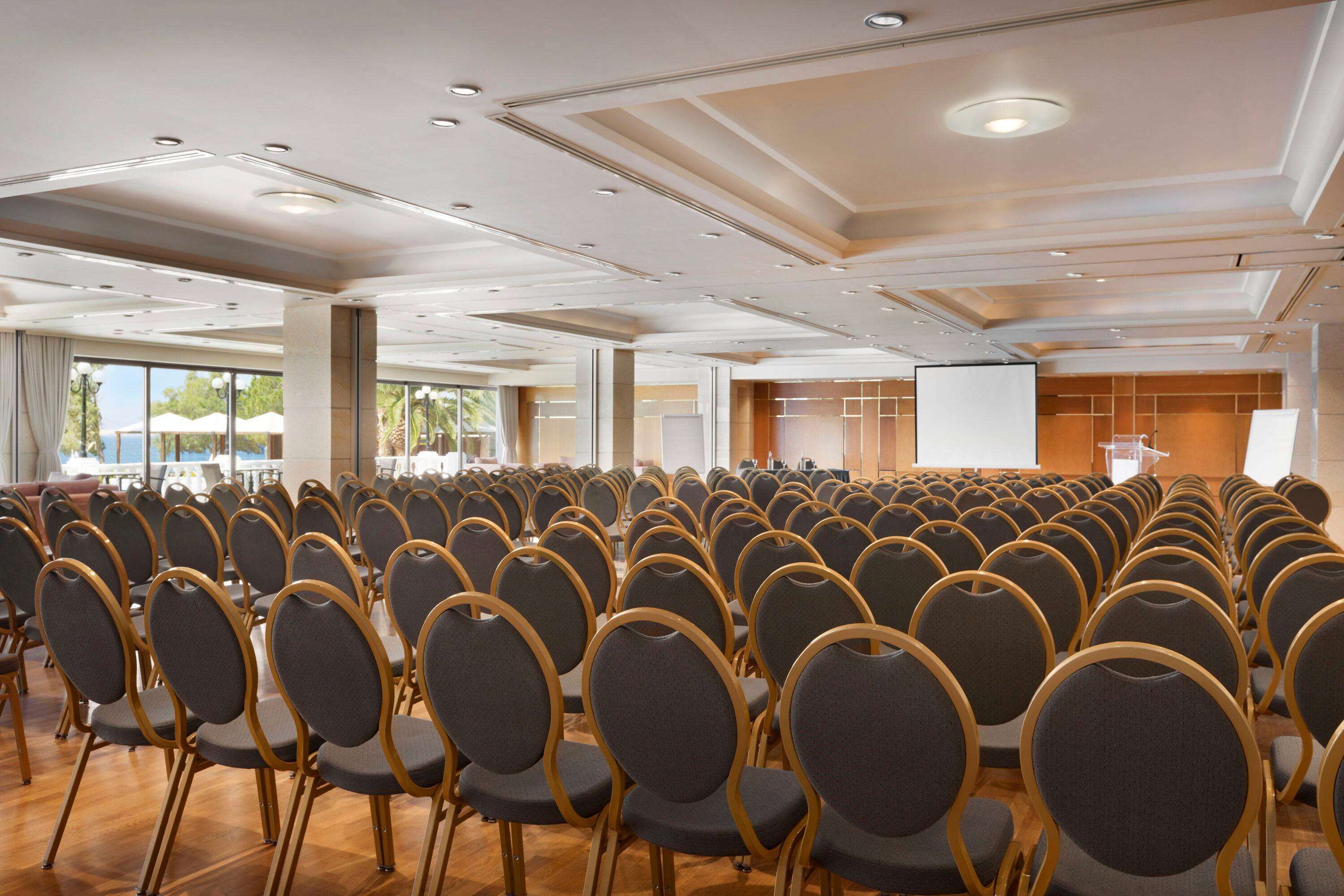 Un salón de conferencias con filas de sillas, un atril y una pantalla de proyector.
