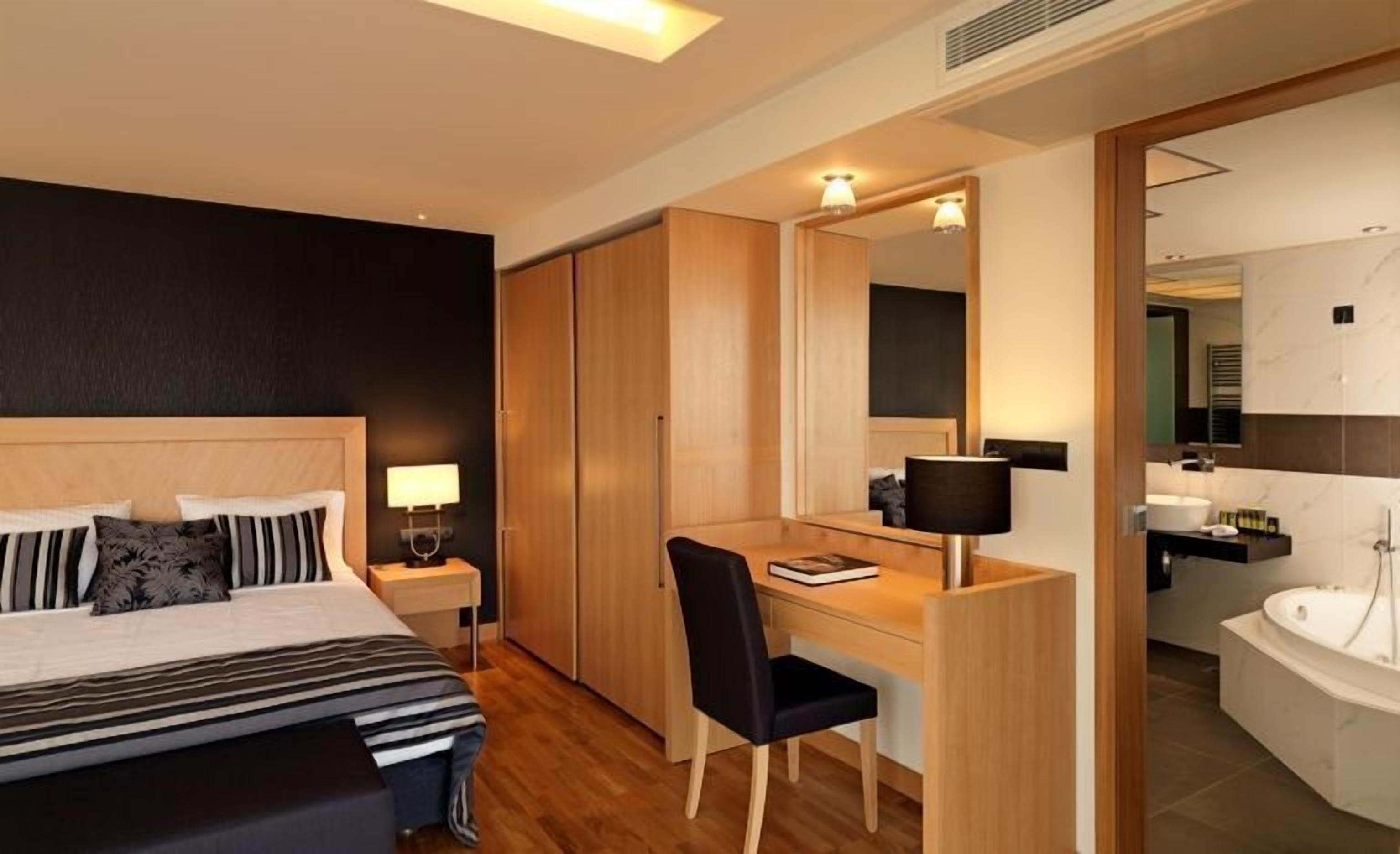 Habitación de hotel con cama, escritorio, silla, espejo y baño con bañera.