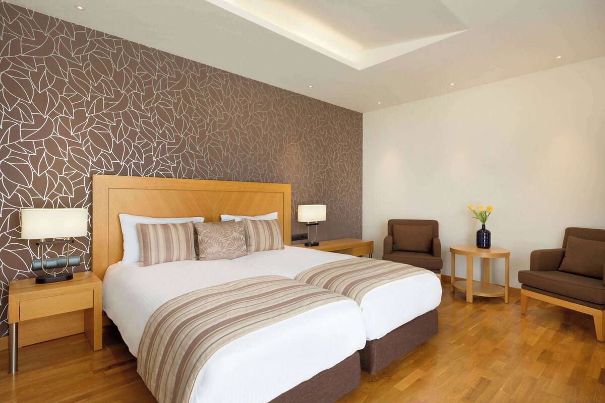 A hotel room with a large bed, two bedside tables, a nightstand, a sofa, and a small side table with a vase of flowers.