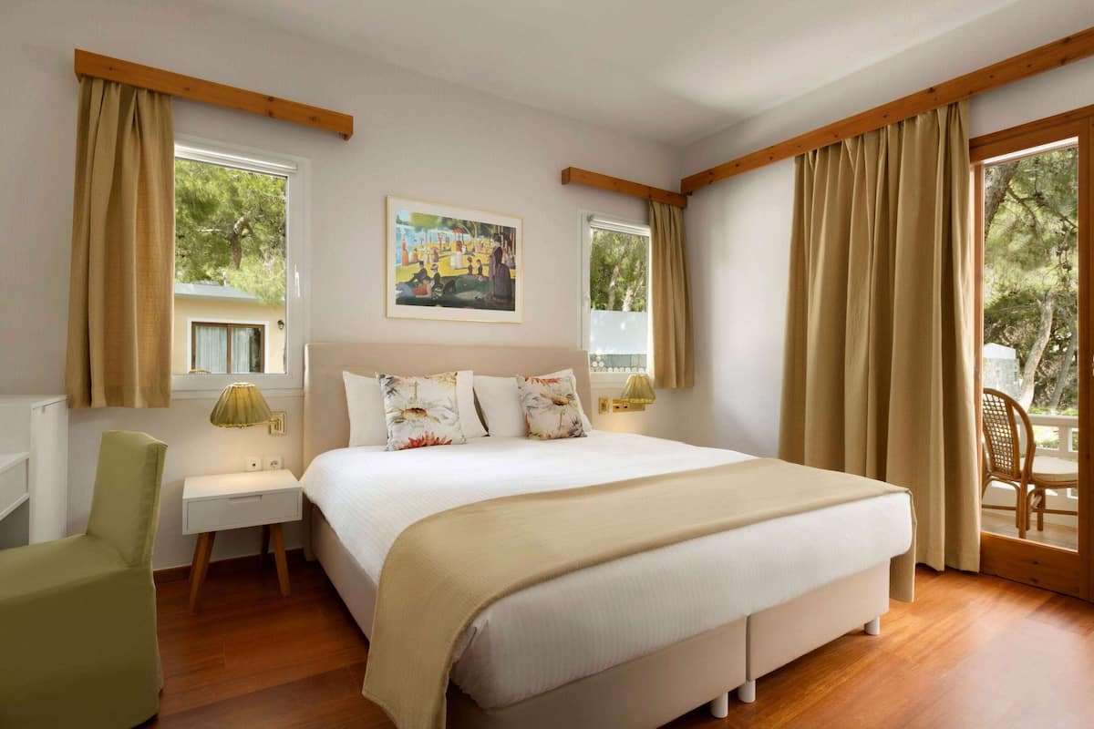 A bedroom with a large bed, two bedside tables, a chair, and a window with curtains.