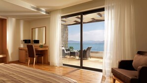 A hotel room with a bed, a desk, a chair, and a sofa. There is a large window with a view of the sea. - Wyndham Loutraki Poseidon Resort (Loutraki-Agioi Theodoroi)