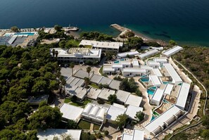 Eine Luftaufnahme eines Küstenhotels mit mehreren Gebäuden, Swimmingpools und einem Strandbereich.