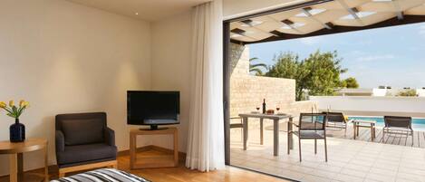 A hotel room with a bed, a TV, a chair, a small table, and a view of an outdoor pool area.