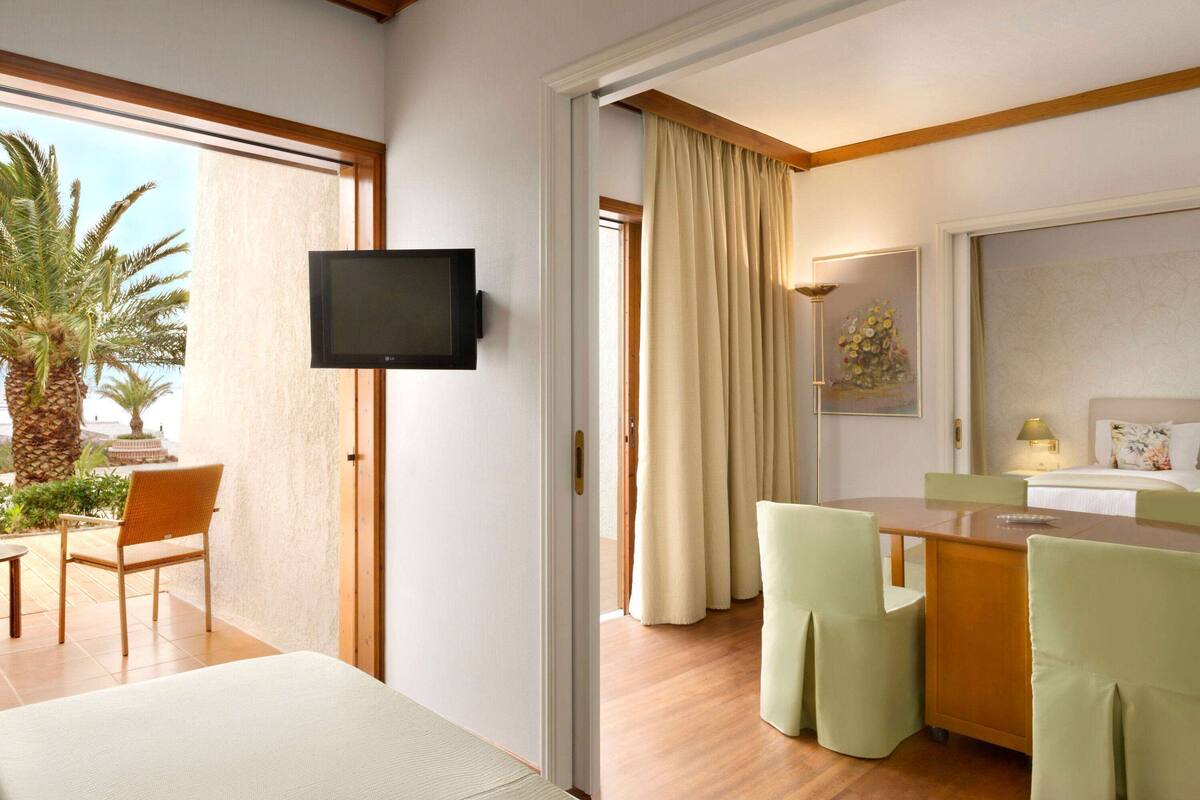 A hotel room with a TV, a dining area with chairs, a bed, and a bathroom with a mirror and sink.