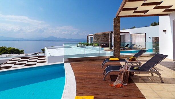 A modern pool area with a clear view of the sea, wooden deck, and lounge chairs. - Wyndham Loutraki Poseidon Resort (Loutraki-Agioi Theodoroi)