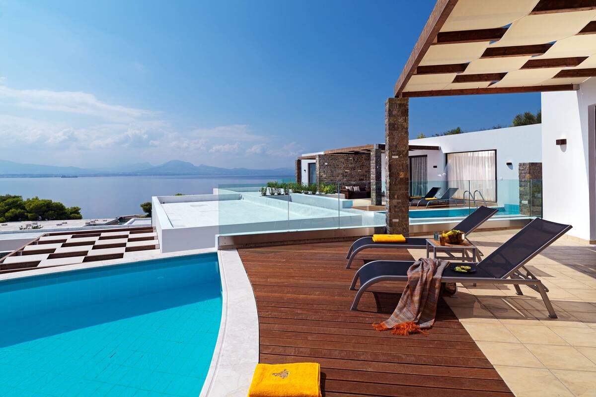 A modern pool area with a clear view of the sea, wooden deck, and lounge chairs.