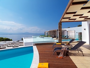 Uma área de piscina moderna com vista clara para o mar, deck de madeira e espreguiçadeiras.