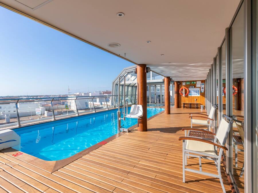 A cruise ship deck with a swimming pool, wooden flooring, and sun loungers.