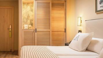 A hotel room with a bed, a nightstand, a lamp, and a wooden wardrobe with a palm leaf design.