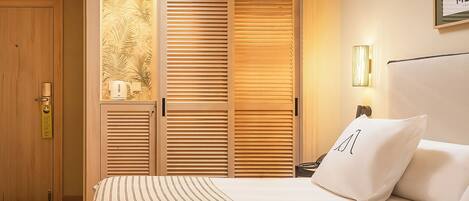 A hotel room with a bed, a nightstand, a lamp, and a wooden wardrobe with a palm leaf design.