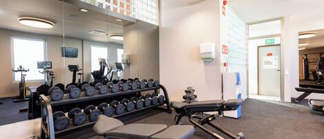 A gym with exercise equipment, a mirror, and a wall-mounted information board.