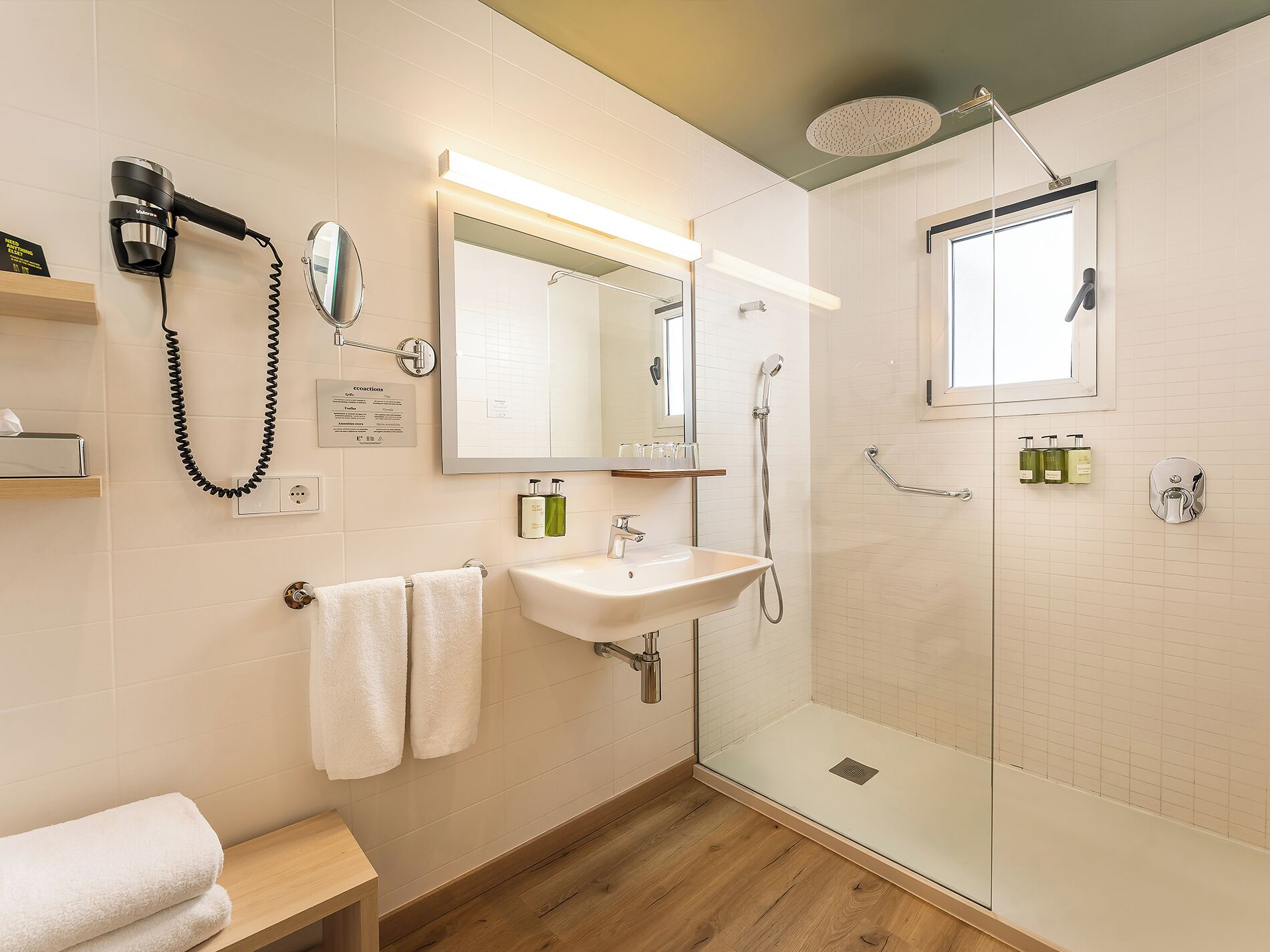 A modern bathroom with a sink, mirror, towel rack, hairdryer, and a glass-enclosed shower.