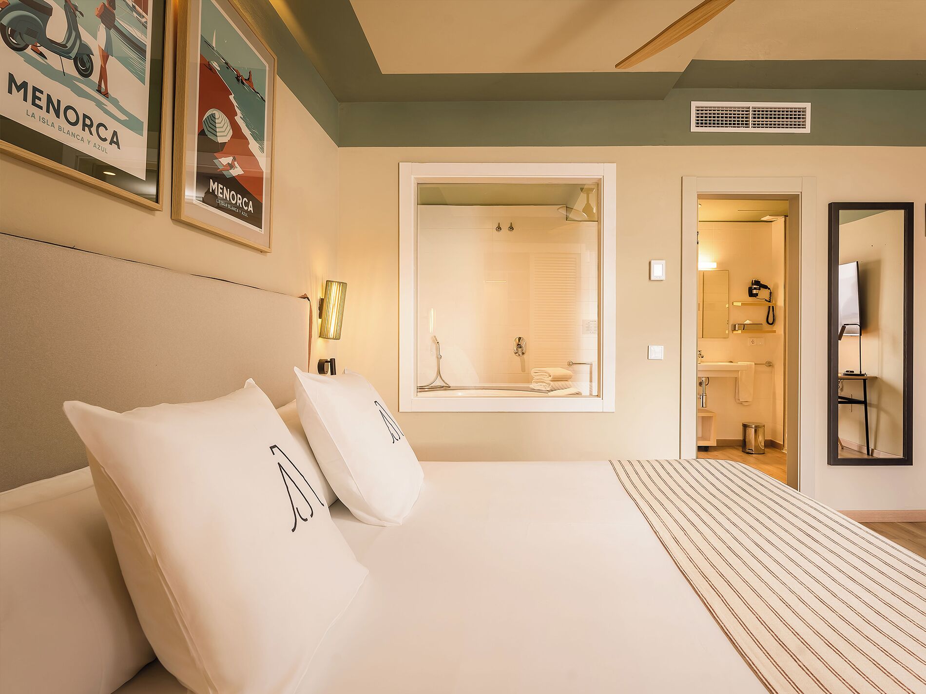 Una habitación de hotel con cama, un espejo grande, ducha y baño con lavamanos e inodoro.