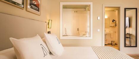 A hotel room with a bed, a large mirror, a shower, and a bathroom with a sink and toilet.