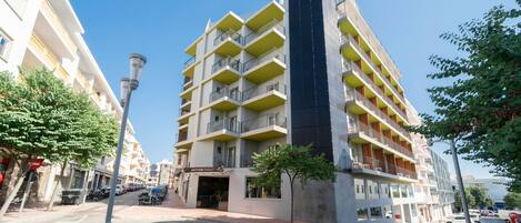 A multi-story hotel with balconies, a central entrance, and a parking area.