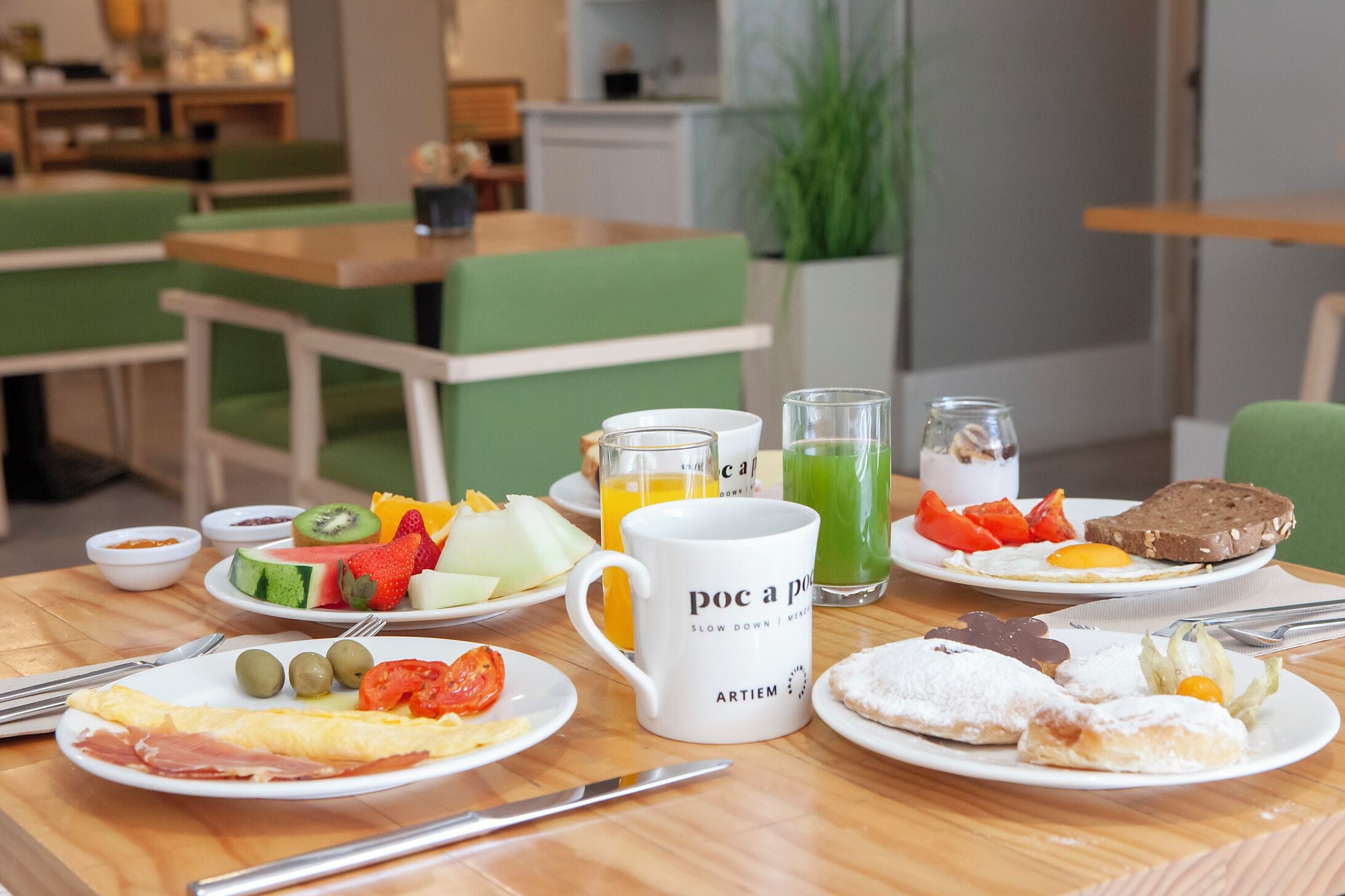 Une table de petit-déjeuner avec divers plats, notamment des œufs, des toasts et des fruits, et une tasse sur laquelle est inscrit le texte « poc a poc ».