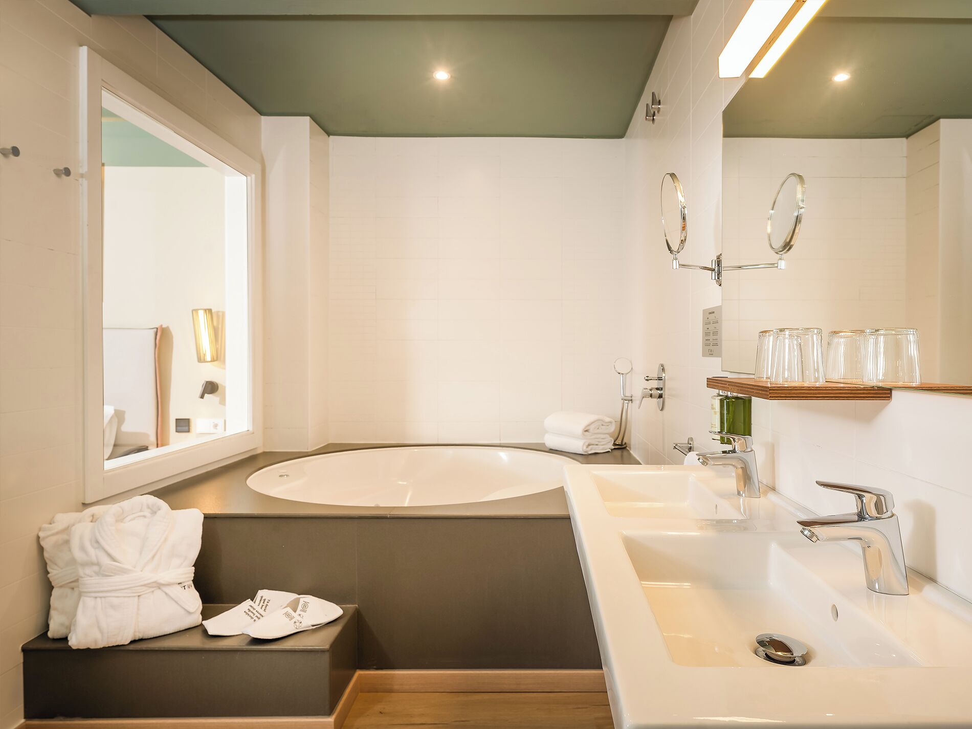 A modern bathroom with a large bathtub, a sink, and a mirror. There are towels and toiletries on the counter.