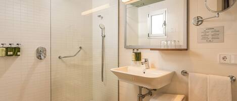 A modern bathroom with a glass-enclosed shower, a sink with a mirror, and a wooden vanity.