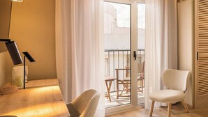 Une pièce comprenant une table en bois, deux chaises, une lampe et une porte-fenêtre coulissante donnant sur un balcon extérieur équipé d’une table et de chaises.
