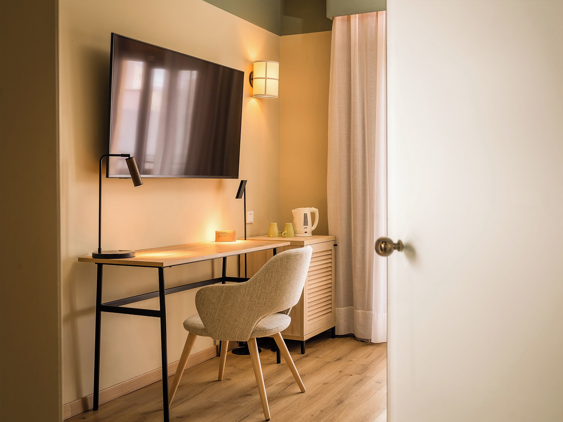 A small, modern room with a desk, chair, flat-screen TV, and a coffee maker.