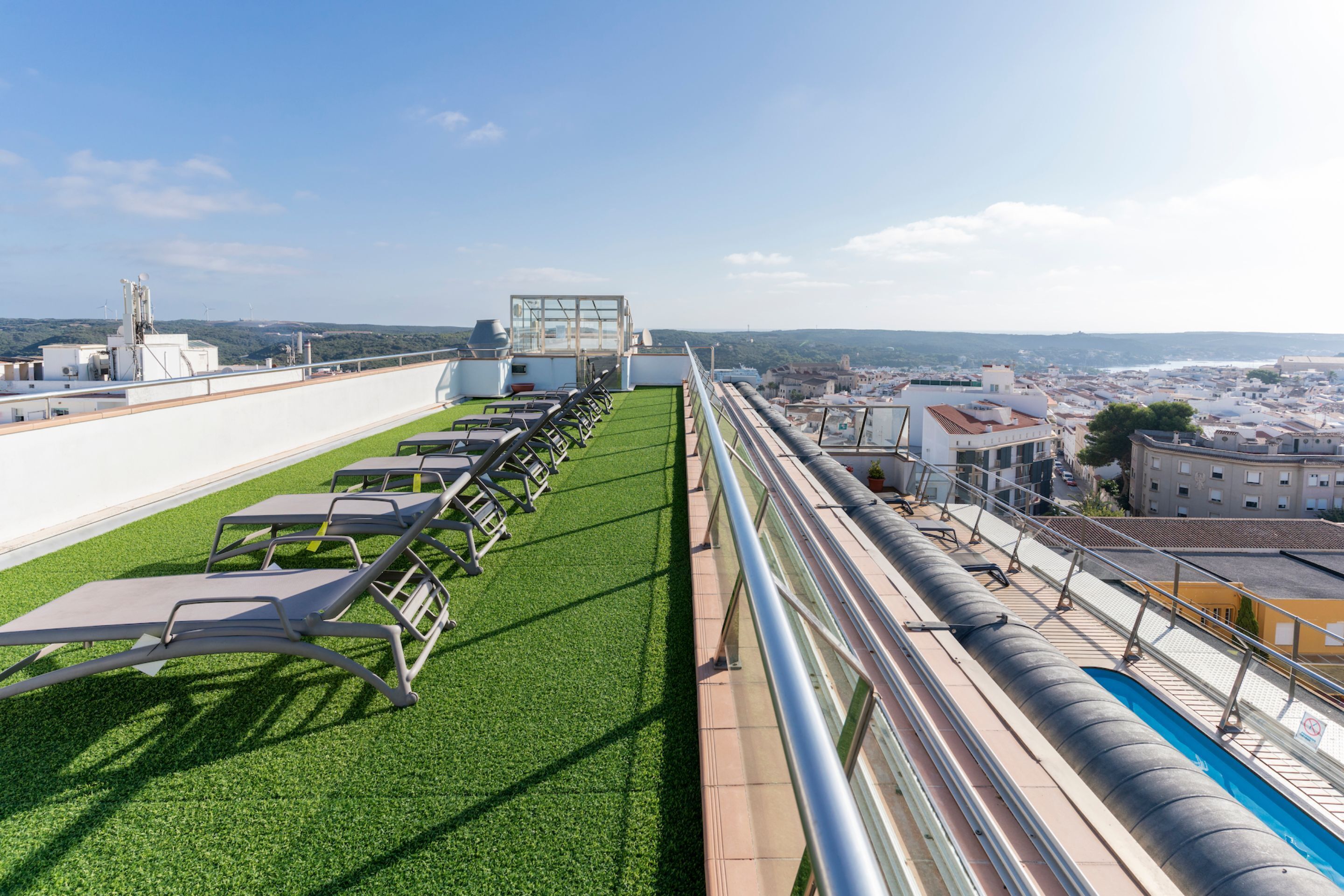 Una terraza en la azotea con césped artificial, tumbonas y una piscina.