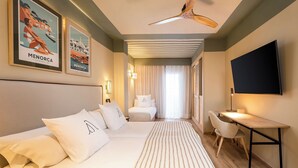 Une chambre d’hôtel avec un grand lit, un bureau, une chaise, un ventilateur de plafond et deux affiches encadrées au mur.