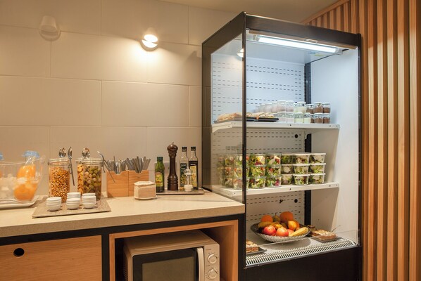 Una cocina con refrigerador lleno de alimentos, microondas y diferentes condimentos y utensilios sobre la encimera.