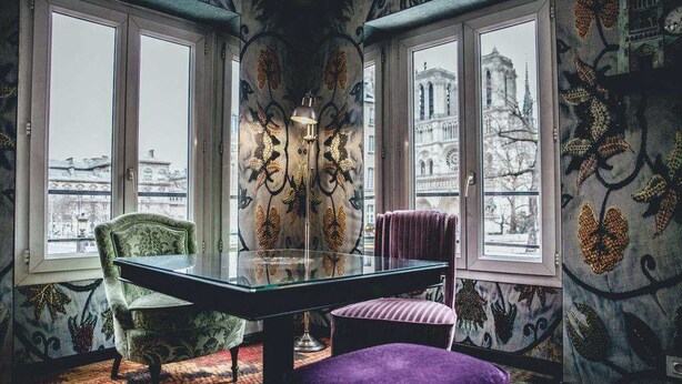 Una habitación con una mesa de vidrio, dos sillas, una lámpara de pie y papel tapiz estampado.