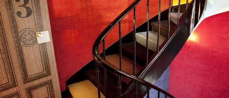 A spiral staircase with a metal railing, carpeted steps, and a red wall.