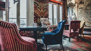 Una habitación con tapicería a rayas y estampados, una silla azul, una silla roja y una mesa con lámpara.