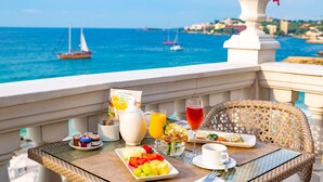 A balcony table with breakfast items, a view of the sea, and a sailboat in the background.