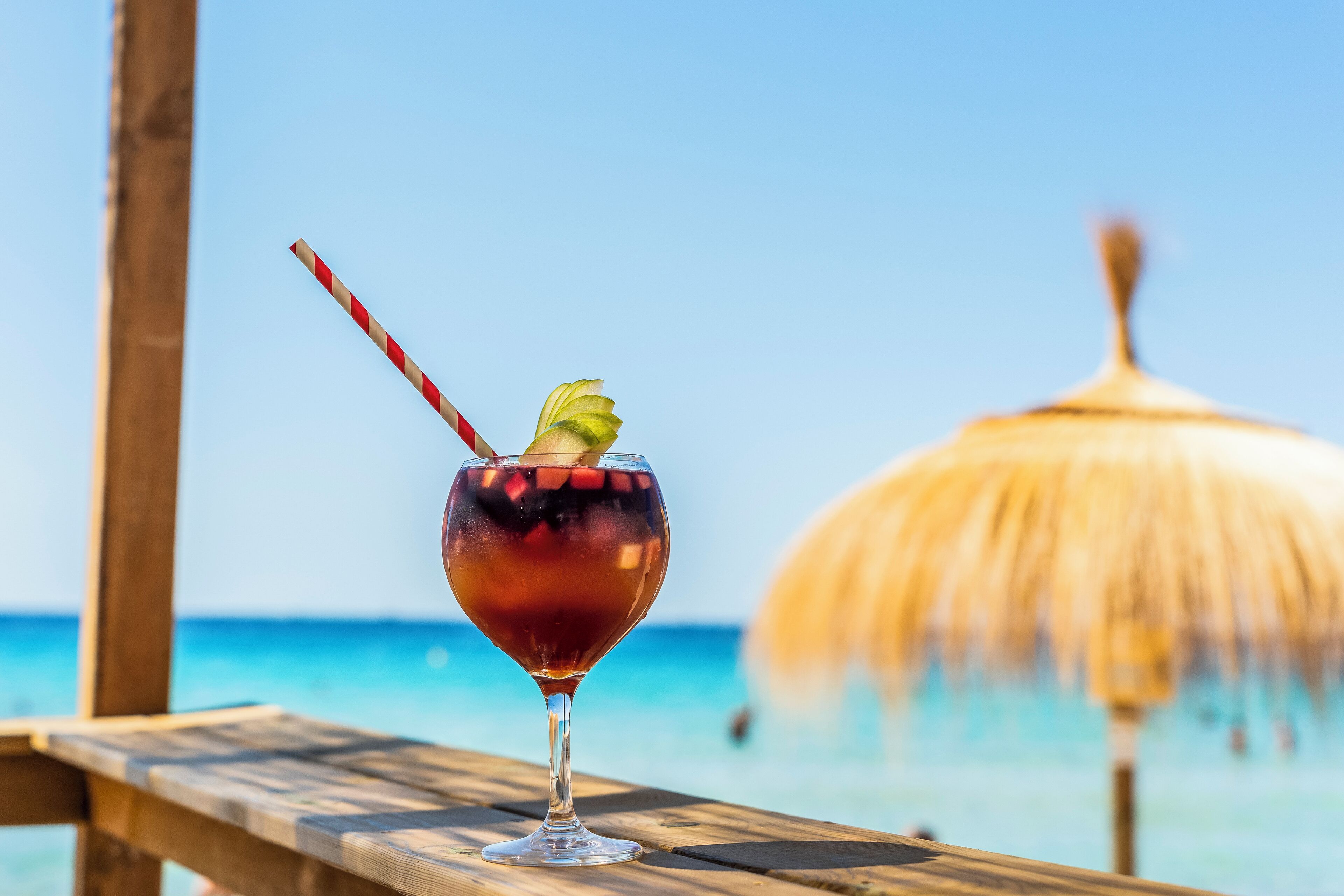 Un vaso de cóctel con pajita en una terraza de madera frente a la playa.