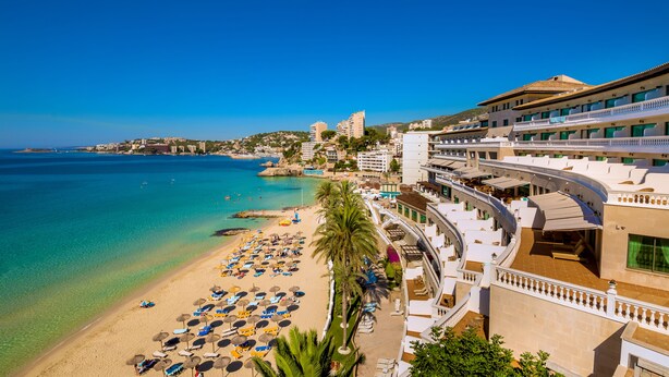 A coastal hotel with a beach view, multiple balconies, and a pool area.