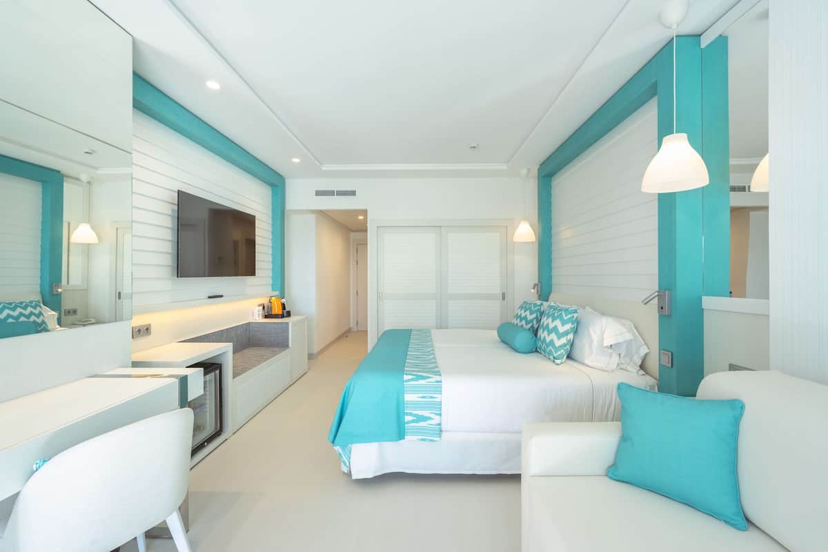 A modern hotel room with a bed, a desk, and a sofa.