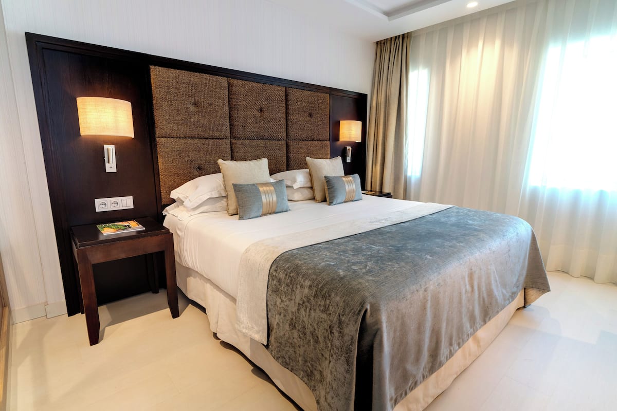 A hotel room with a large bed, two bedside tables, a nightstand, and a wall-mounted lamp.