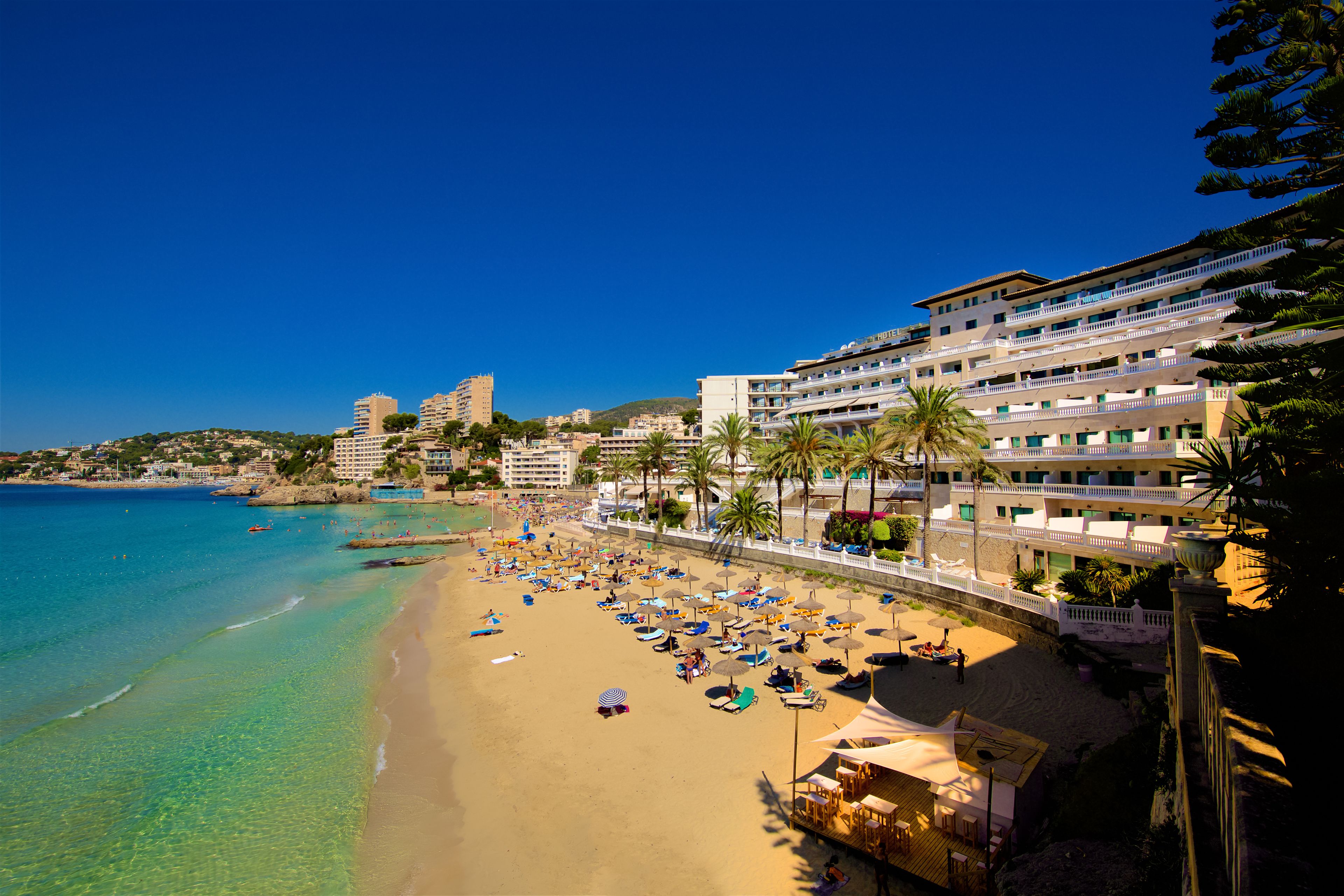 A beachside hotel with multiple balconies, a sandy beach, and clear blue water.
