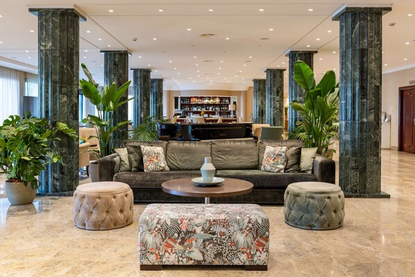 A spacious lobby with a bar area, large columns, and plush seating.