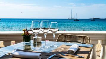 A table set with wine glasses, a salt shaker, and cutlery on a balcony overlooking the sea with boats in the distance.