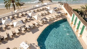 A resort pool with clear blue water, surrounded by lounge chairs and umbrellas, overlooking a beach and ocean.