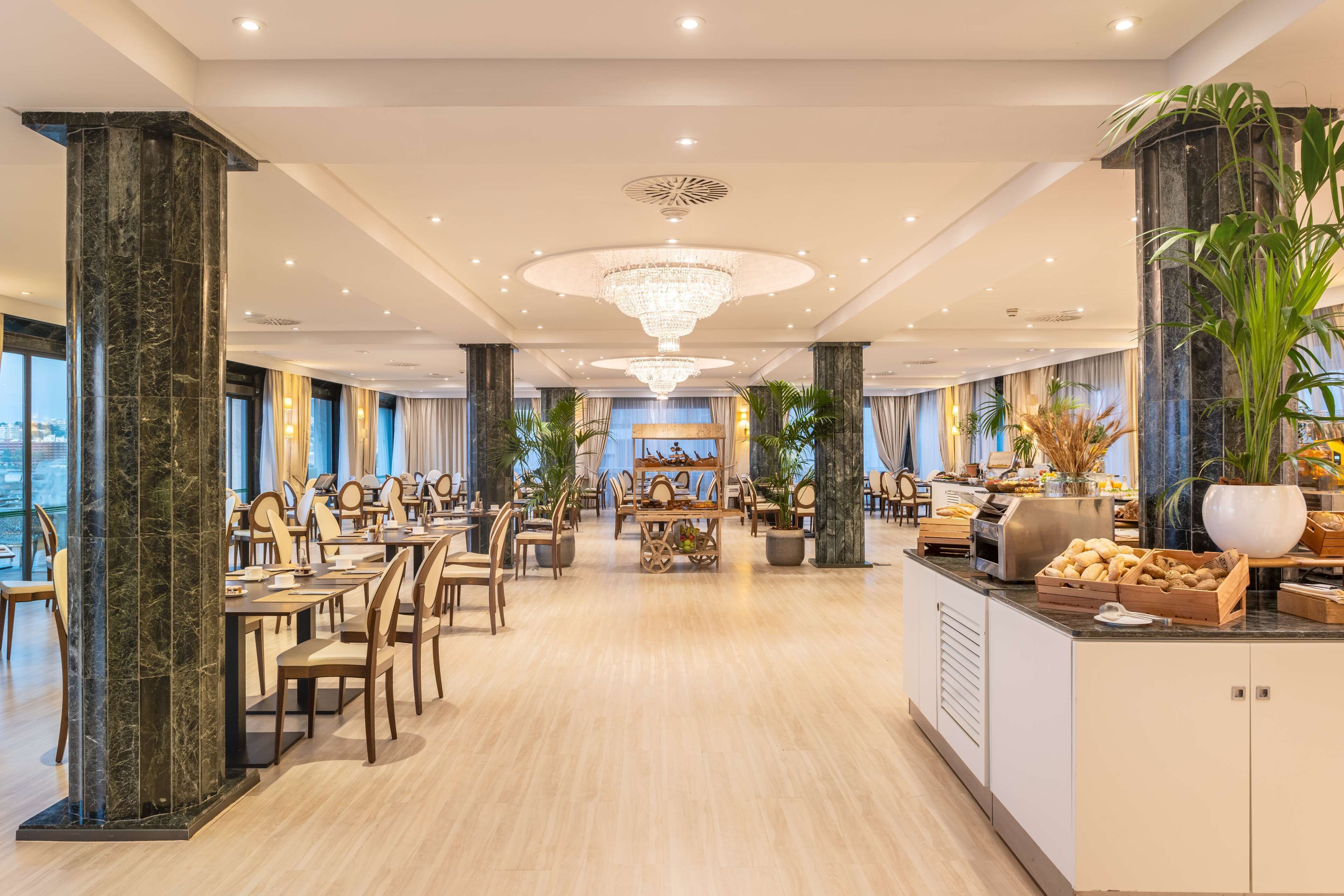 A spacious dining area with marble columns, chandeliers, and a central buffet.
