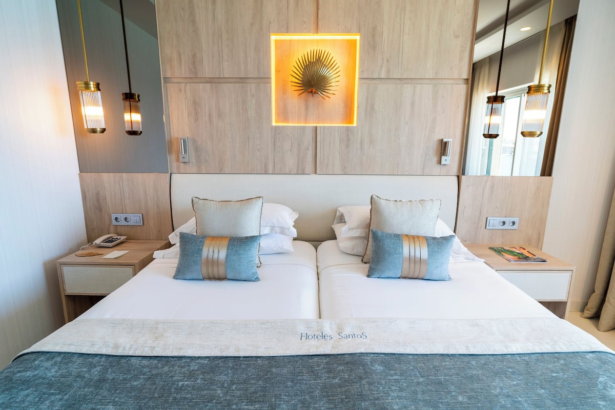 A double bed with two pillows, a bedside table with a phone, and a wall-mounted light fixture.