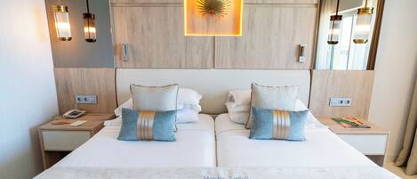Uma cama de casal com duas almofadas, mesa de cabeceira com telefone e luminária fixada na parede.