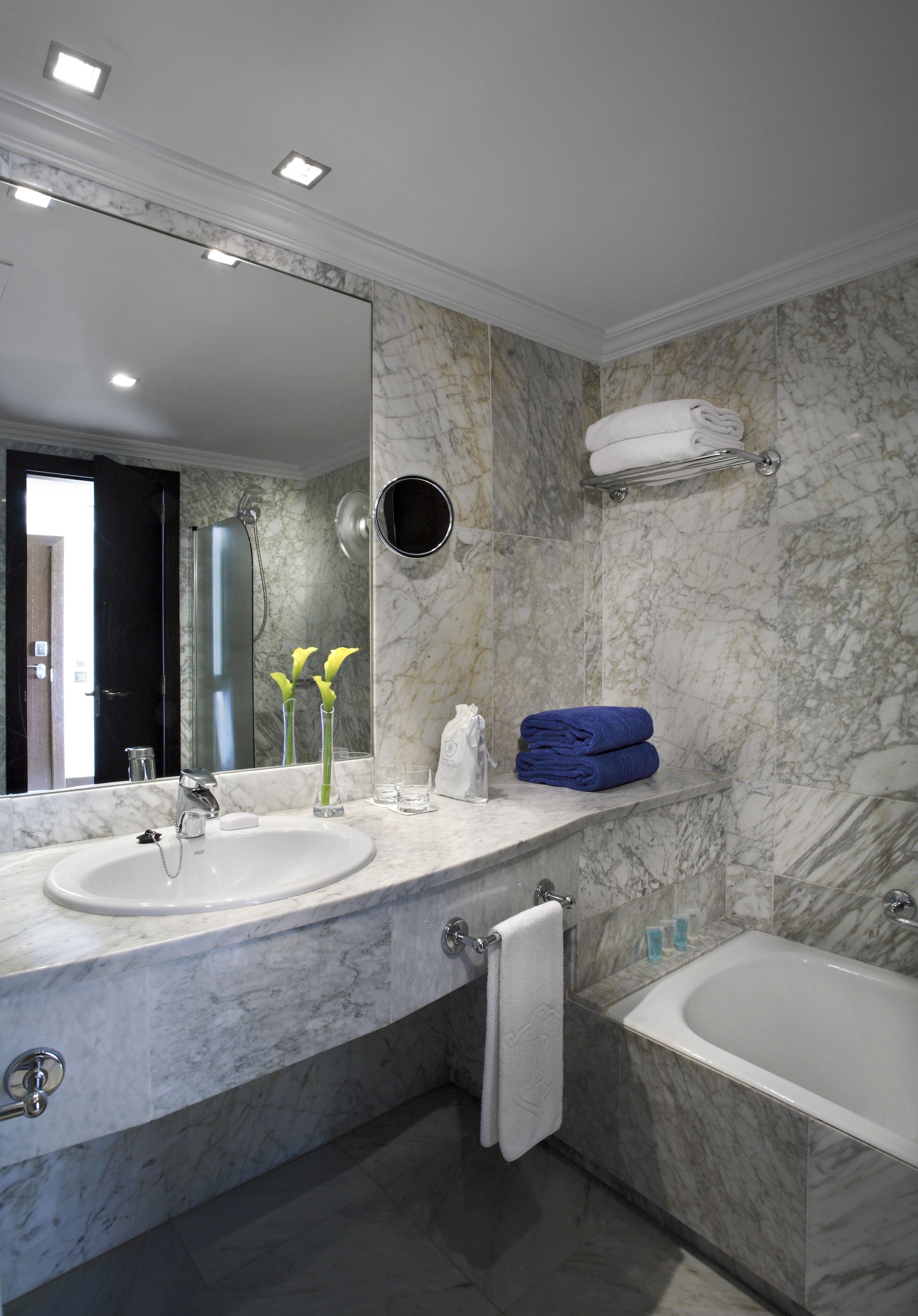 Une salle de bain moderne avec deux vasques, un grand miroir, une baignoire et des murs en marbre.