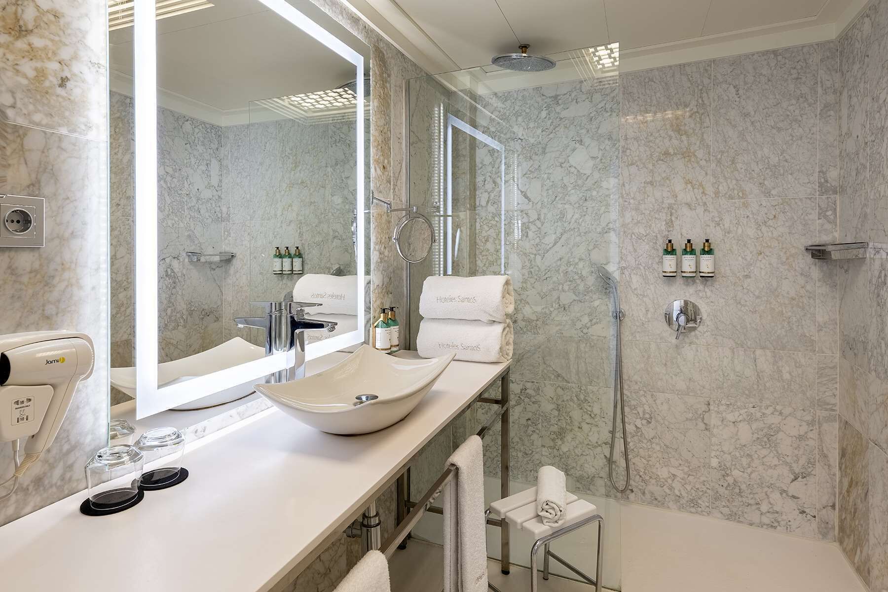 Un baño moderno con un espejo grande, un lavamanos tipo recipiente, un cabezal de ducha de mano y un perchero para toallas.