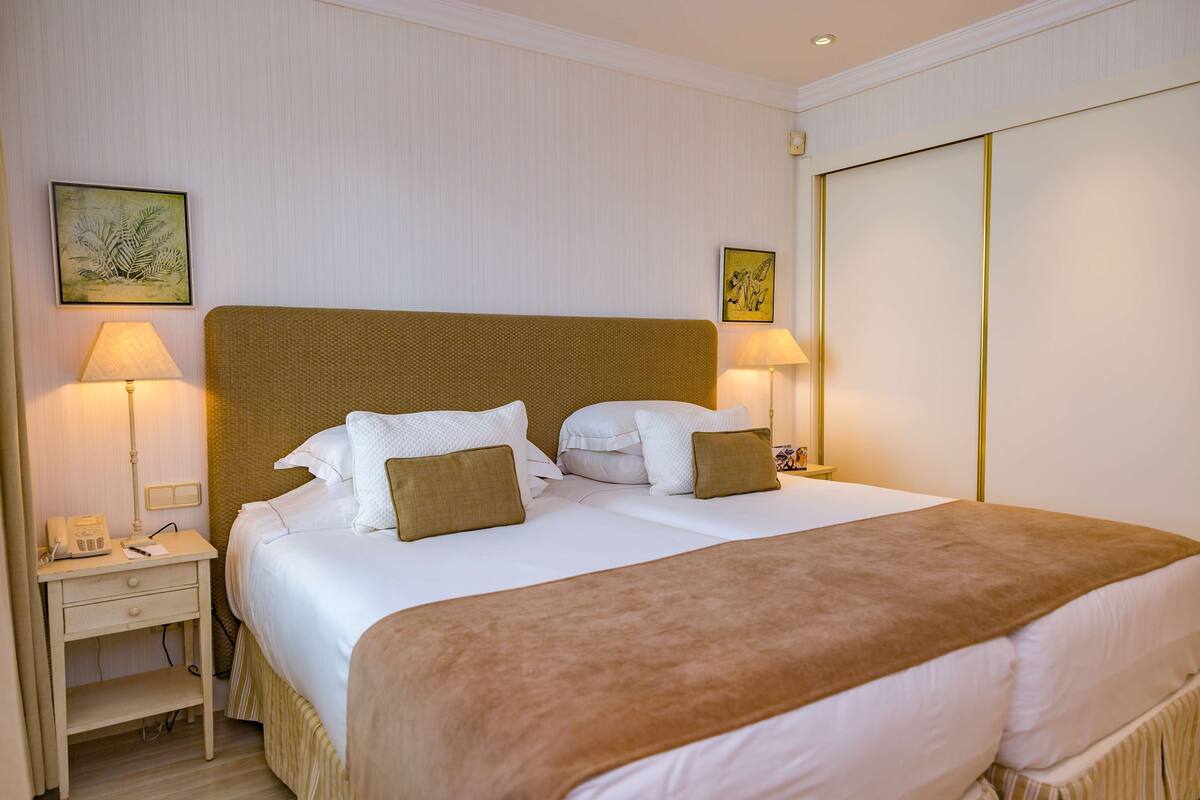 A neatly made double bed with a brown throw blanket, two bedside lamps, and a nightstand with a telephone.
