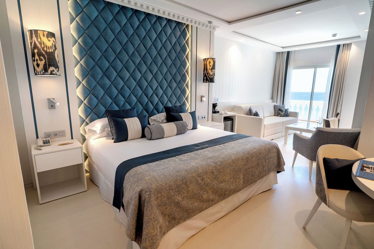A modern hotel room with a large bed, a seating area, and a balcony with a view.