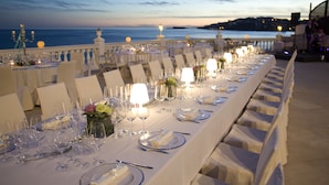 Una larga mesa de comedor dispuesta para un evento formal, con vista al mar.