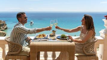 Una pareja brindando con copas de vino en una mesa con vistas al mar.