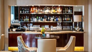 Una zona de bar con una mesa redonda y dos sillas, un jarrón con flores y una estantería bien surtida al fondo.