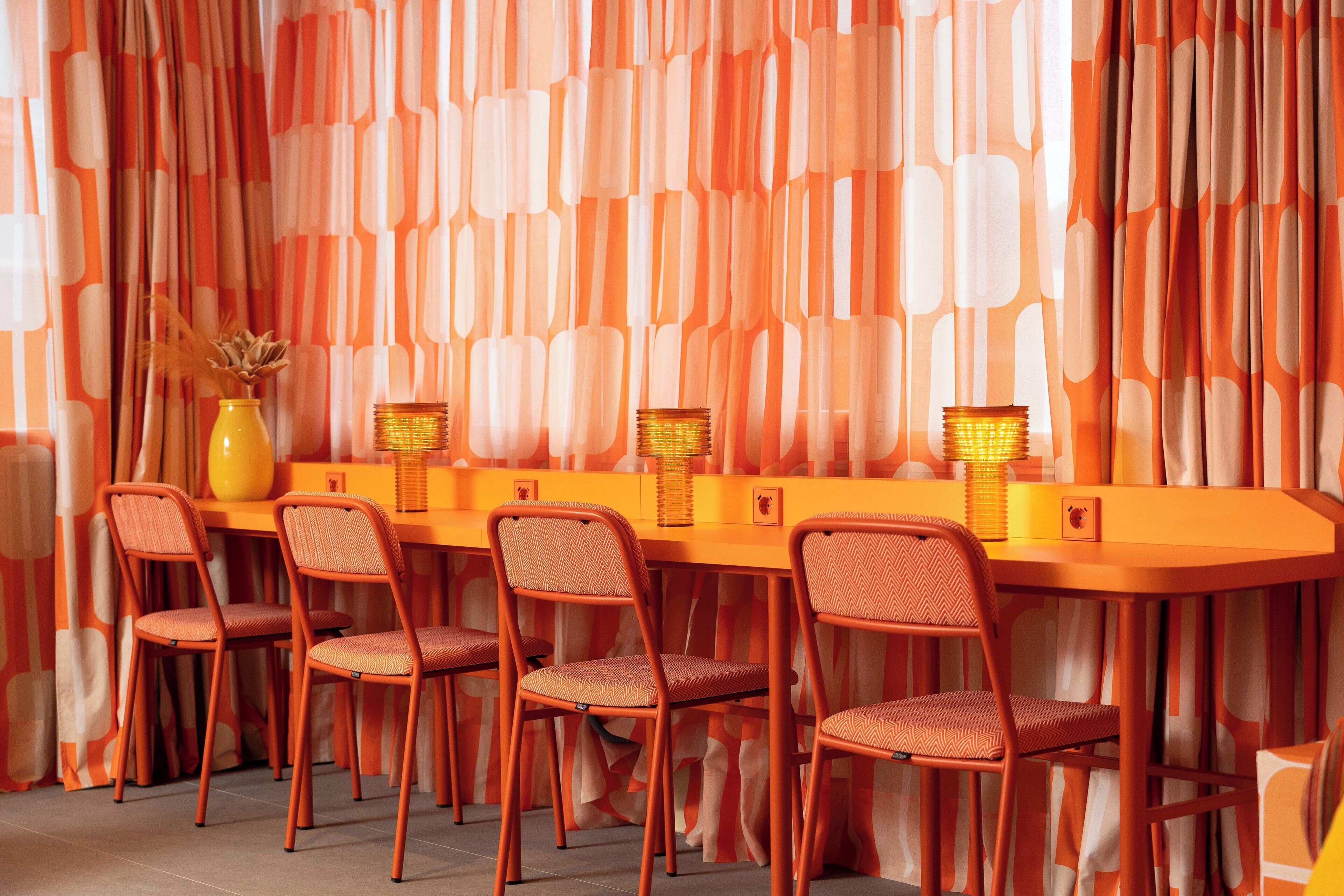 A dining area with a long table, six chairs, and orange curtains.